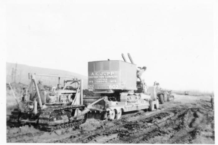 Caterpillar pushing loaded lowbed trailer through muddy road, Alaska Highway, B.C. 1943-1944